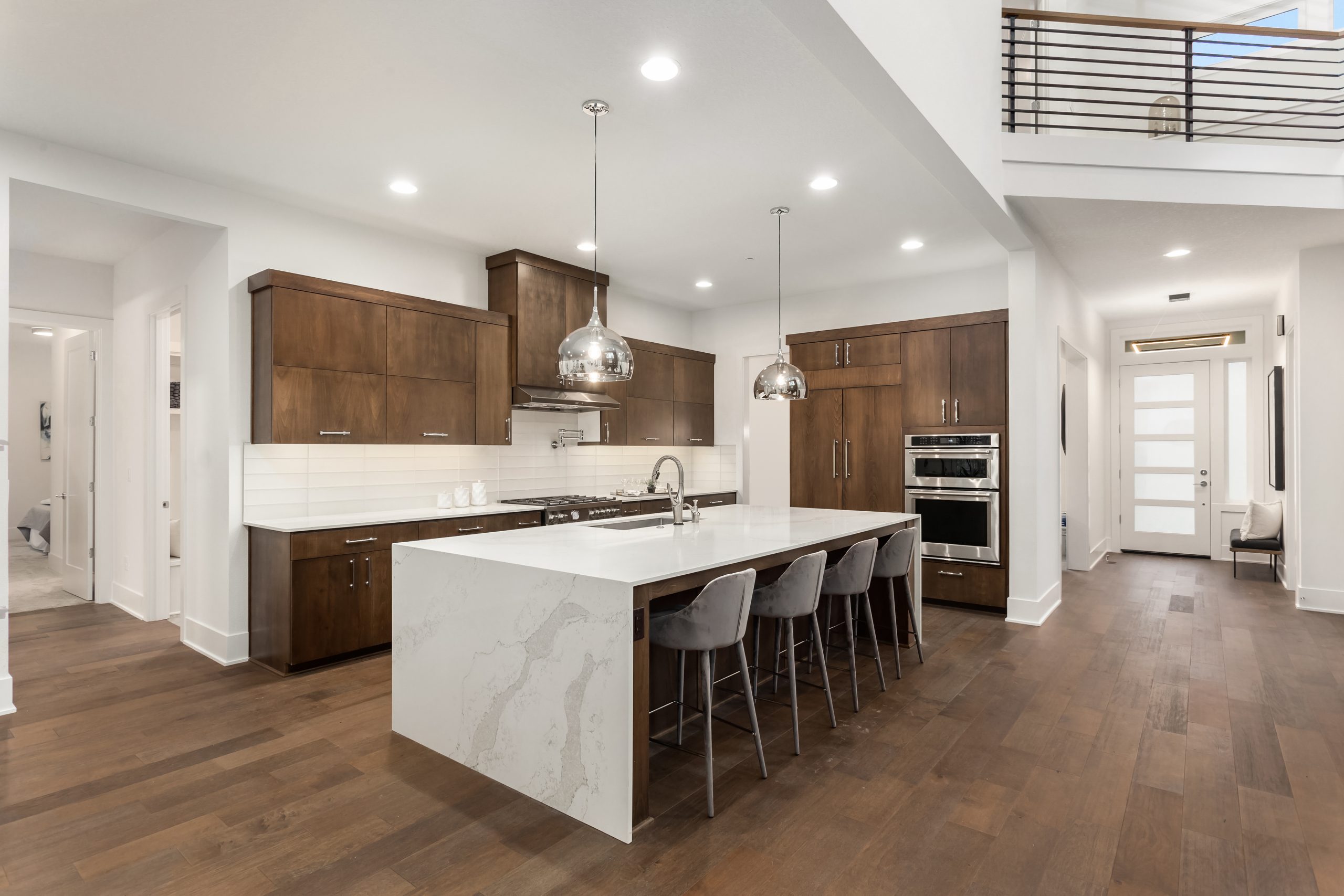 Beautiful kitchen in new luxury home with island, pendant lights, and hardwood floors. Features quartz waterfall island with dark cabinets and stainless steel appliances.